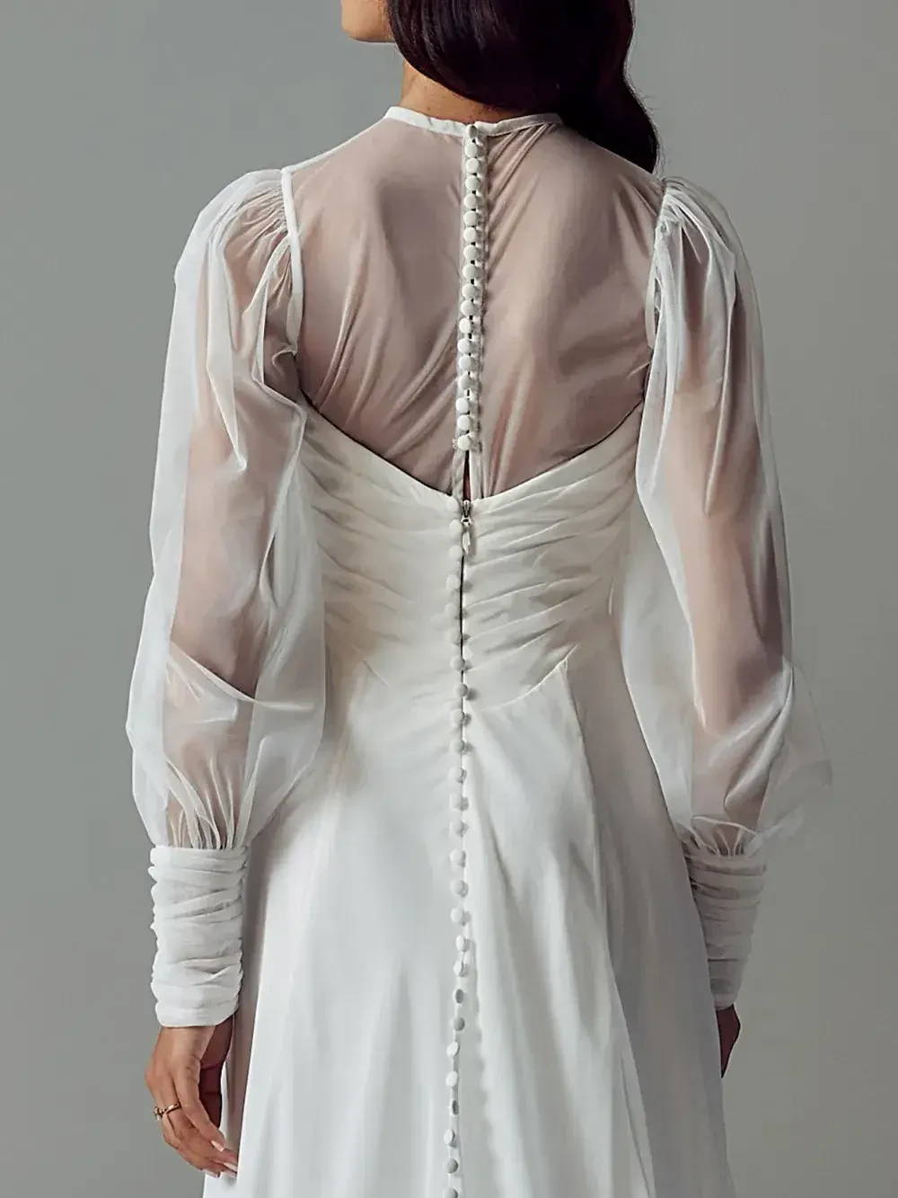 A woman wearing a white dress with sheer, puffed sleeves and a buttoned back.