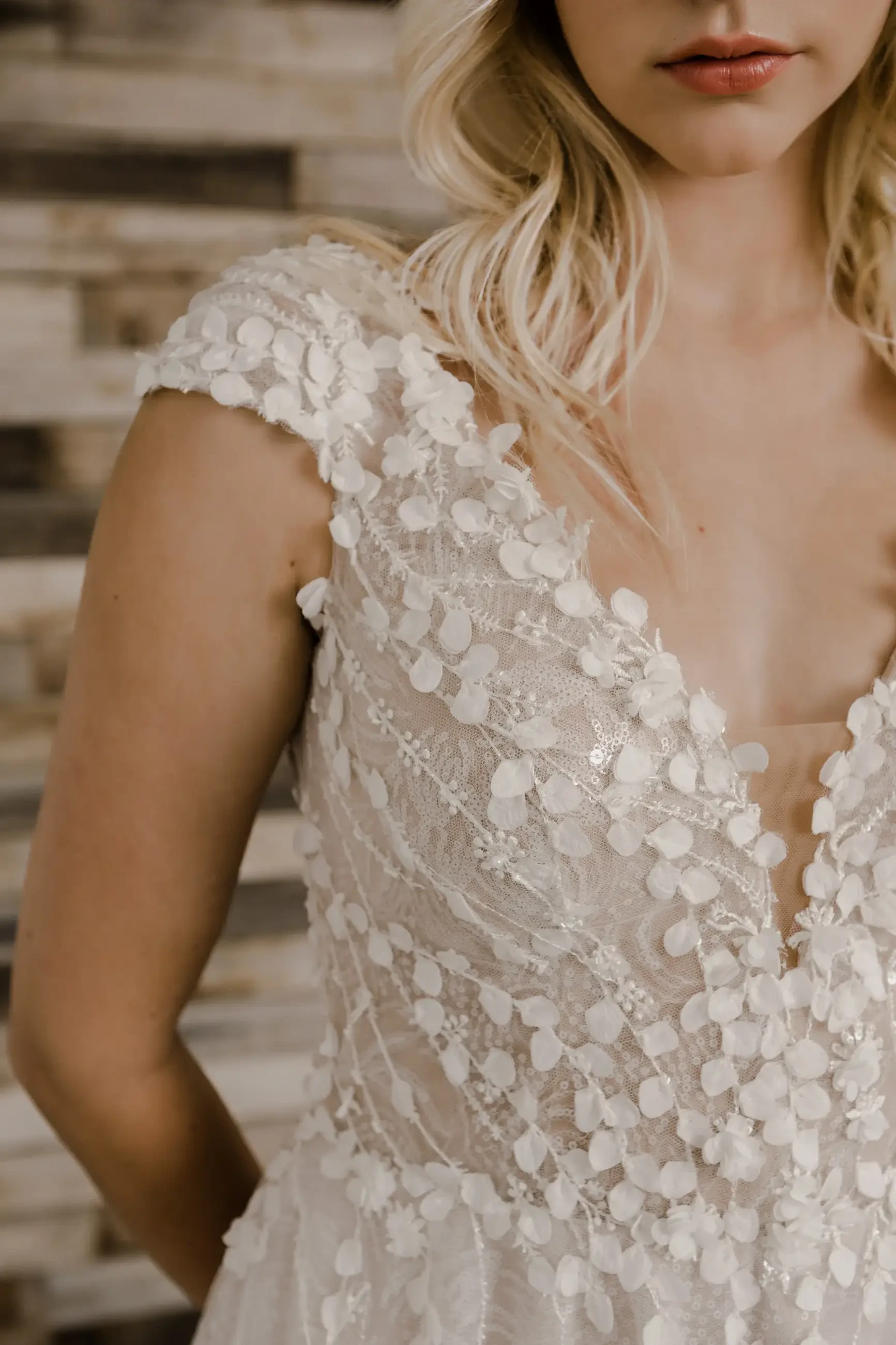 Close-up of a bride in a detailed lace wedding dress with floral applique. Her neutral expression and soft blonde waves create an elegant and serene tone.
