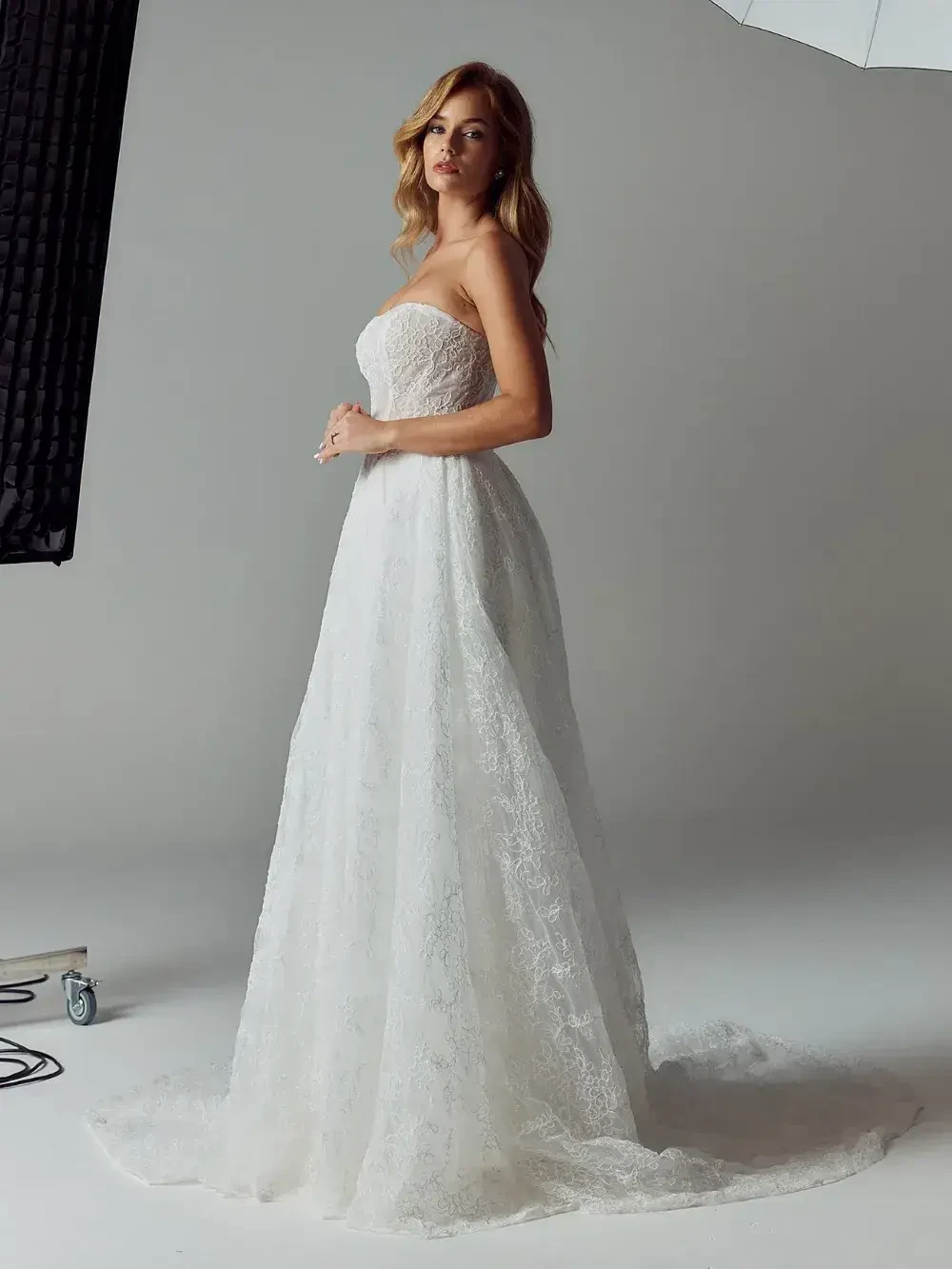 A woman in a strapless white wedding dress standing in a photo studio.