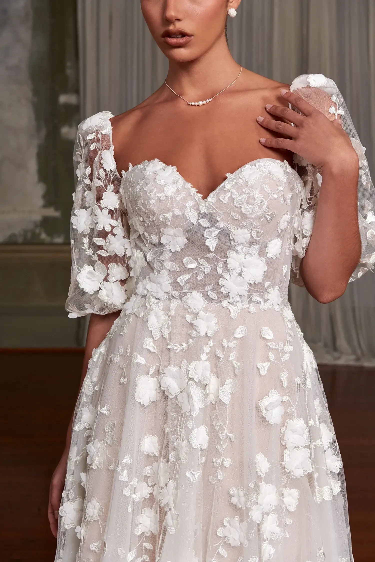 A close-up of a woman wearing a light-colored dress adorned with floral appliqu&eacute;s, featuring puff sleeves and a sweetheart neckline.