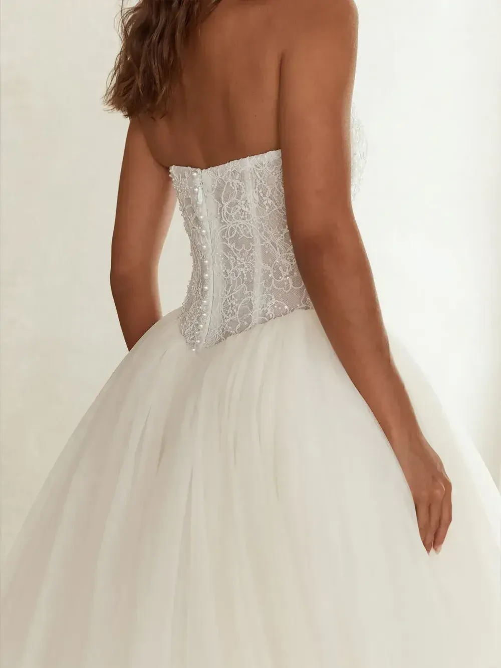 A woman in a strapless wedding dress with a lace bodice and a full tulle skirt, seen from the back.