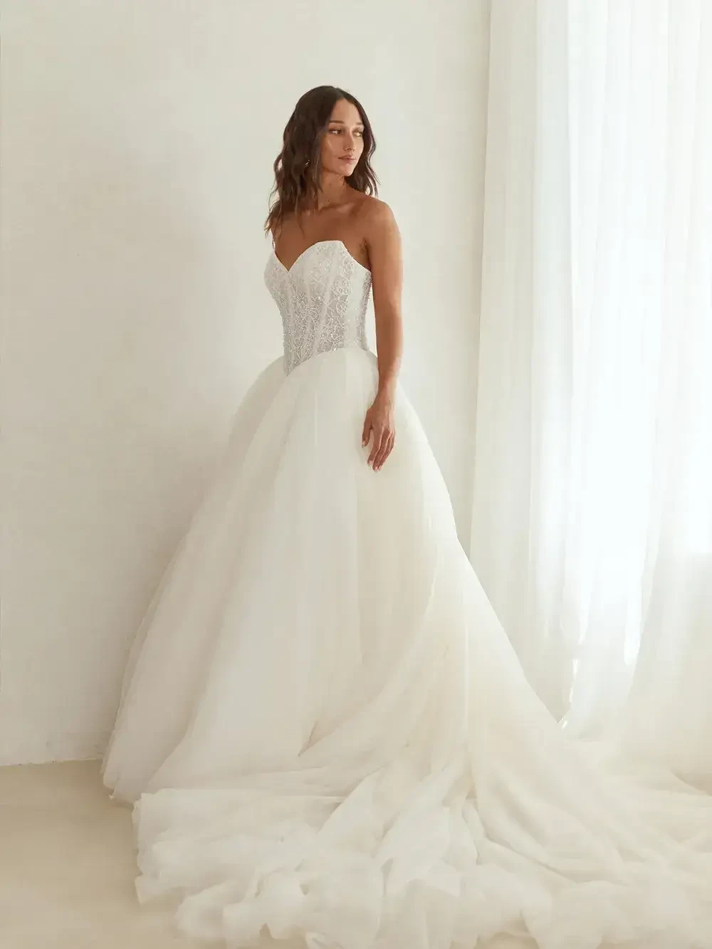 A woman in a beautiful white wedding dress with a fitted bodice and a full skirt, standing against a light background.